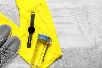Sports leggings, shoes, bottle for water and smartwatch on light background