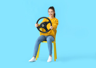 Fototapeta na wymiar Young woman with steering wheel sitting in chair on color background