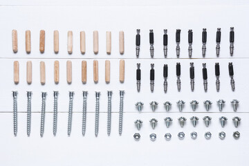 Set of bolts, nuts and dowels on white wooden background