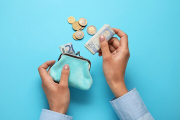 Woman putting money into wallet on blue background - obrazy, fototapety, plakaty