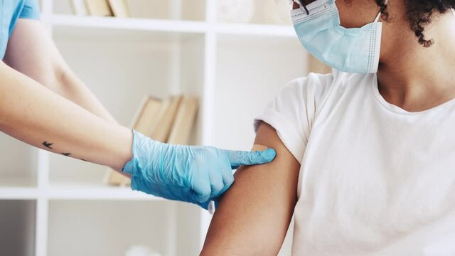 Coronavirus vaccine. Flu shot. Pandemic prevention. Female doctor in gloves sticking plaster after covid-19 jab to Arab male patient shoulder.