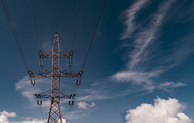 View through white clouds on a high-voltage pole against a blue sky. Electricity, technology