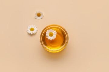 Bowl of sweet honey and chamomile flowers on color background