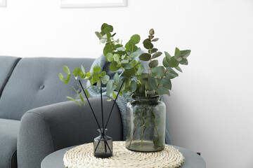 Vase with eucalyptus branches and reed diffuser on table near light wall
