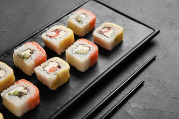 Board with delicious sushi rolls and chopsticks on dark background, closeup