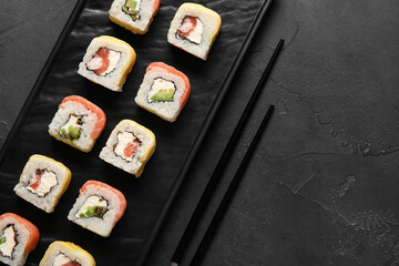 Board with delicious sushi rolls and chopsticks on dark background, closeup