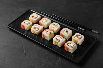 Board with set of delicious sushi rolls and chopsticks on dark background