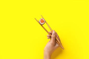 Woman holding chopsticks with delicious maki roll on color background © Pixel-Shot