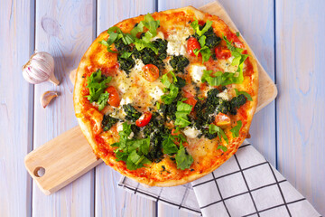 Pizza with with spinach, mozzarella, cherry tomatoes and garlic on wooden table.