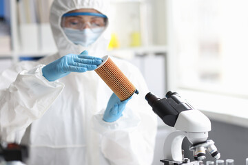 Scientist in protective suit holds filter cartridge in laboratory