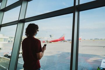 Long hair man in mask with smartphone in the airport with plane on the background