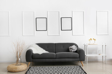 Dark comfy sofa near light wall with blank poster frames