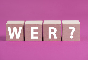 The word who is standing in german language on wooden cubes, pink colored background