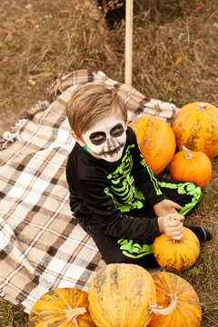 boy in skeleton costume with face painting in the park with pumpkin