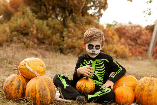 boy in skeleton costume with face painting in the park with pumpkin
