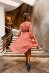 beautiful blonde woman in pink dress with makeup and hairstyling  with lights and lamps indoor portrait back view. young woman spining  in stylish interior. girl looks festive on party