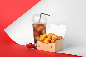 Paper box with fried popcorn chicken and plastic cup of cola on color background