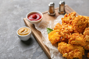 Board with tasty popcorn chicken, sauces and spices on grey background, closeup