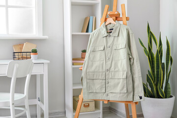 Easel with stylish green jacket in light room
