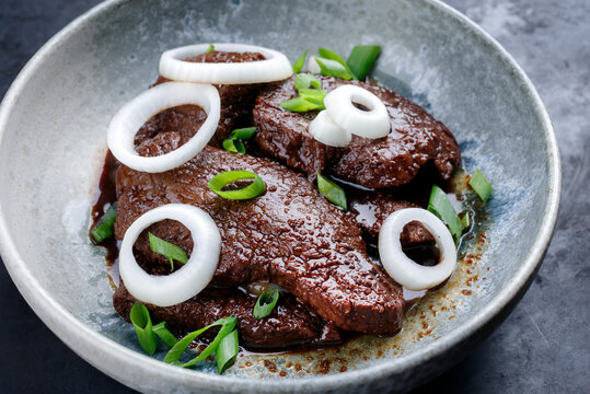 Modern style traditional Cuban dry aged angus bistec encebollado steak with onion rings in soy sauce served as close-up in a Nordic design bowl