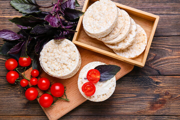 Composition with crispy rice crackers, tomato and basil on wooden background