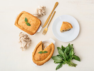 Baking dishes and plate with tasty mushroom pot pie on white wooden background