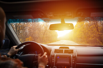 man driving a car on an autumn road at sunset. Close-up of hands on a steering wheel. view from the driver's back. empty road. view from the car