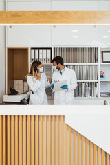 Young practitioners or technicians with face protective masks working together at clinic reception desk.