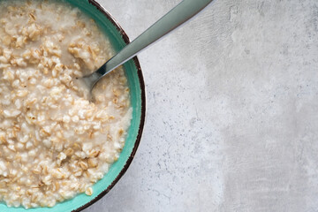 A green bowl of cooked oats porridge with a spoon, healthy breakfast and dieting product close up with copy space