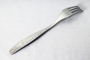 inverted silver fork on white cloth background, close-up