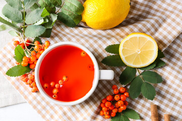 Composition with cup of tasty rowan tea, lemon and berries on fabric background, closeup