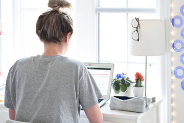 Young teen girl student sitting at desk in her room studying using laptop computer 