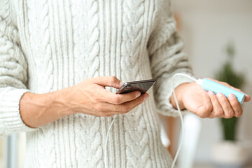 Young man with phone and power bank at home, closeup