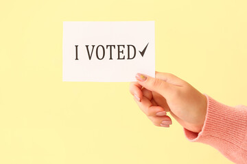 Hand holding paper with text I VOTED on color background