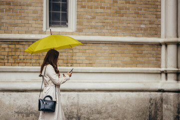 Woman using a smartphone and holding a yellow umbrella while out in the city