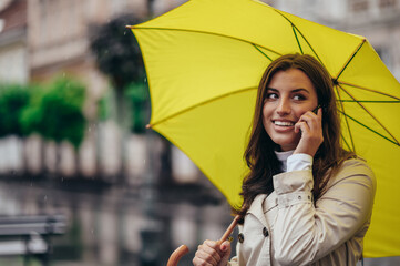 Woman using a smartphone and holding a yellow umbrella while out in the city