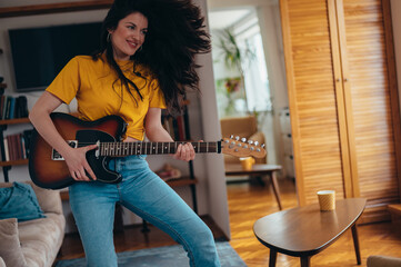 Young cheerful woman playing electrical guitar at home
