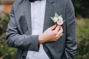 The groom in a gray suit straightens the boutonniere on his jacket with his hand. Wedding portrait.