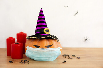 Halloween concept. Pumpkin Jack with face mask and witch hat next to red candles and spiders