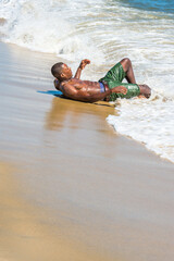 A well built young sexy black guy, half naked, whole body wet,  is lying on the beach, play with rolling and foamed waves.
