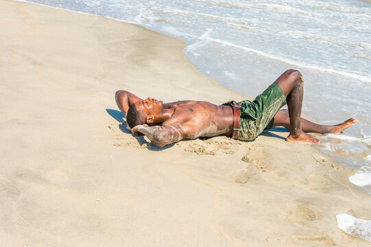 A well built young sexy black guy, half naked, whole body wet,  is lying on the beach, relaxing..