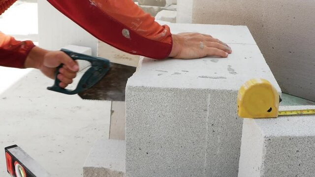 A builder cuts white brick blocks with a saw. Building a house from a white brick block