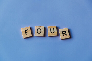 Number four laid out from tiles in words. Wooden tiles on a blue background with letters. View from above. Copy space.