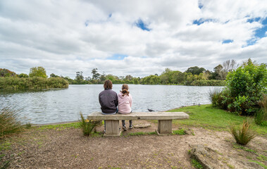 Brother and Sister Sitting on Park Bench in Front of a Lake in Auckland New Zealand - with copy space