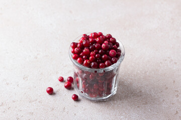 Glass with fresh raw cranberries on light beige textured background