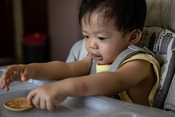Adorable joyful and Happy 1years old Chinese baby boy having food while sit on baby chair