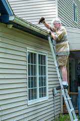 Man on  a ladder cleaning out gutters of his house
