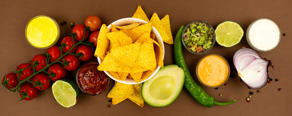 A plate of nachos corn chips with sauces and ingredients, red onion, avacado, peppers and tomatoes.