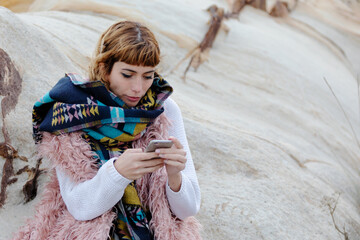 A young blonde woman sing a cell phone in a beach in winter