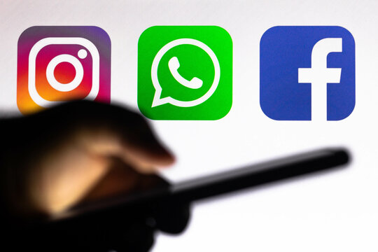 October 5, 2021, Brazil. In this photo illustration the Instagram, WhatsApp and Facebook logo app seen in the background of a silhouette hand holding a mobile phone.